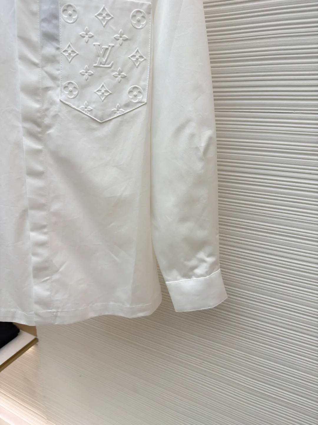 LOUIS VUITTON Embossed Pocket Lapel Shirt ●Original version: Purchased and developed for 3989 ●Item number: 1681491-B05 ●Fabric: Cotton twill woven fabric ●Technology: Concave embossed printing ●Color: white ●Version: Fitted version ●Weight: about 370 grams ●Size: XS-S-M-L ●Description: The twill pattern is obvious on the front of the fabric and blurry on the reverse. Single yarn is used in both warp and weft directions, and the linear density is close. The warp density of the fabric is slightly higher than the weft density, and the hand feel is relatively soft. The fabric has excellent stability, is not easy to deform, and prevents bulging; cotton fiber has good hygroscopicity, which keeps the fabric in a water balance, making people feel comfortable, and adding to the sophistication of the fabric. The concave and convex embossing process is formed by heating and shaping the upper and lower dies. The rollers press the fabric at a certain temperature, and the three-dimensional hierarchical convex surface is produced through mechanical embossing. The fabric produces a concave and convex pattern with a relief-style three-dimensional effect and a special gloss effect. The three-dimensional shape, pattern and text have a strong three-dimensional sense, adding a decorative art effect, clear layers, concentrated three-dimensional image, and accurate perspective angle. The collar can be adjusted with buttons for both formality and comfort; the pleats and tabs at the back are classic shirting techniques, with the pleats providing extra room for movement and the tabs keeping the shirt in shape when hanging. The button front uses custom-fit buttons that are positioned accordingly, and together these details ensure the shirt's functionality and crisp look. The overall wiring is straight and delicate, the fabric is comfortable and soft, and the color is consistent without color difference. It can be matched with the same style to create a fashionable look and control various occasions. Customized accessories, complete with three standards, same style for men and women!